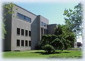 Gray building with rectangular windows and a grassy lawn, under a clear blue sky.