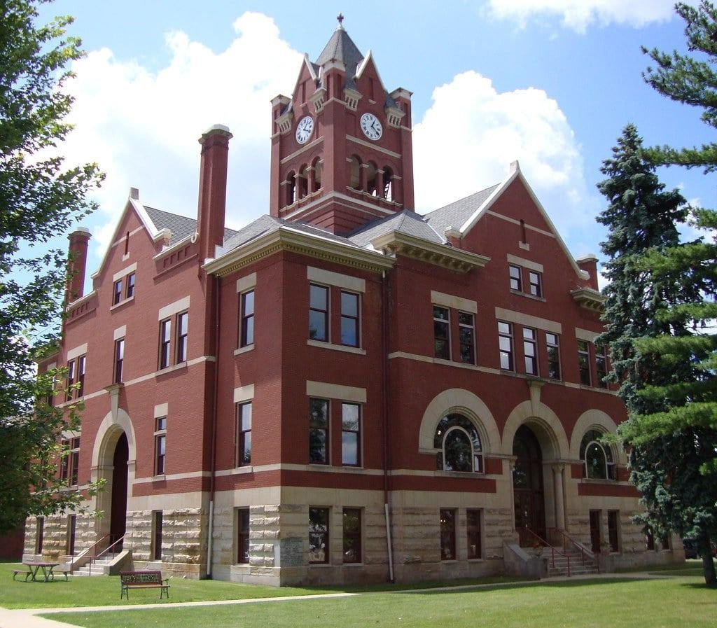 Red brick courthouse with clock tower and stone foundation against a blue sky.