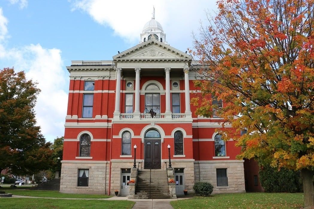 Red brick courthouse with white columns, cupola, and fall foliage.