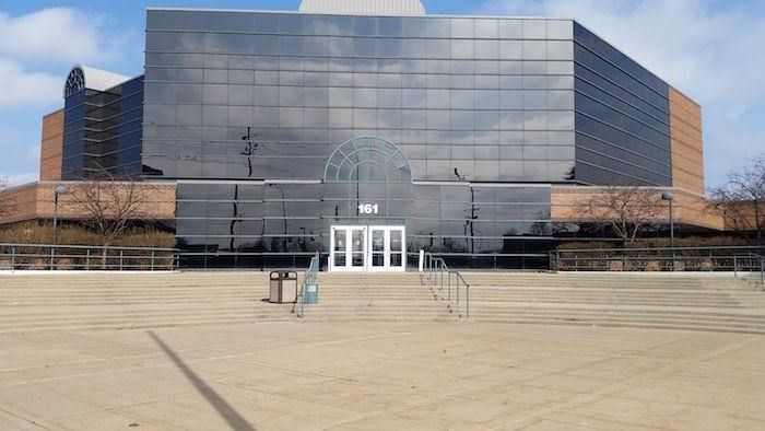 Large building with reflective glass facade, brick sides, and a concrete plaza.