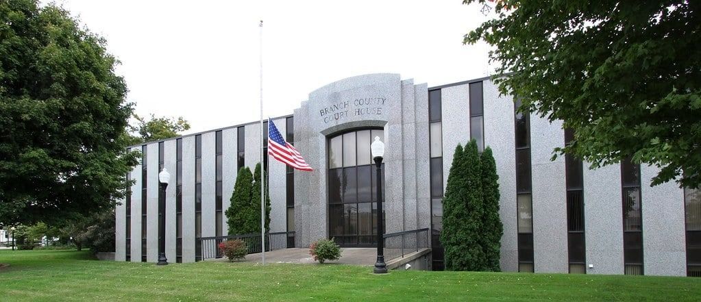 Exterior of a courthouse with an American flag. The building is gray and white with a lawn.