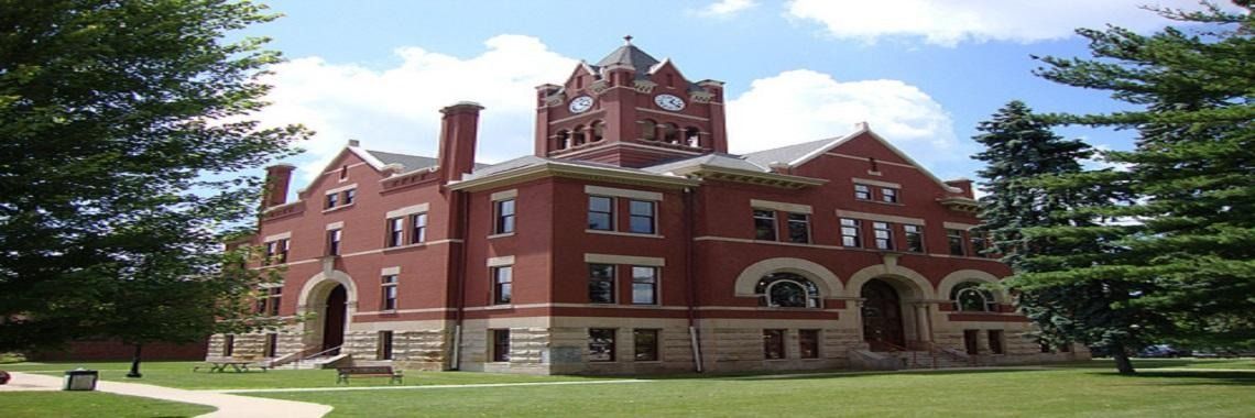 Red brick building with a tower, set on a green lawn with trees and a cloudy sky.
