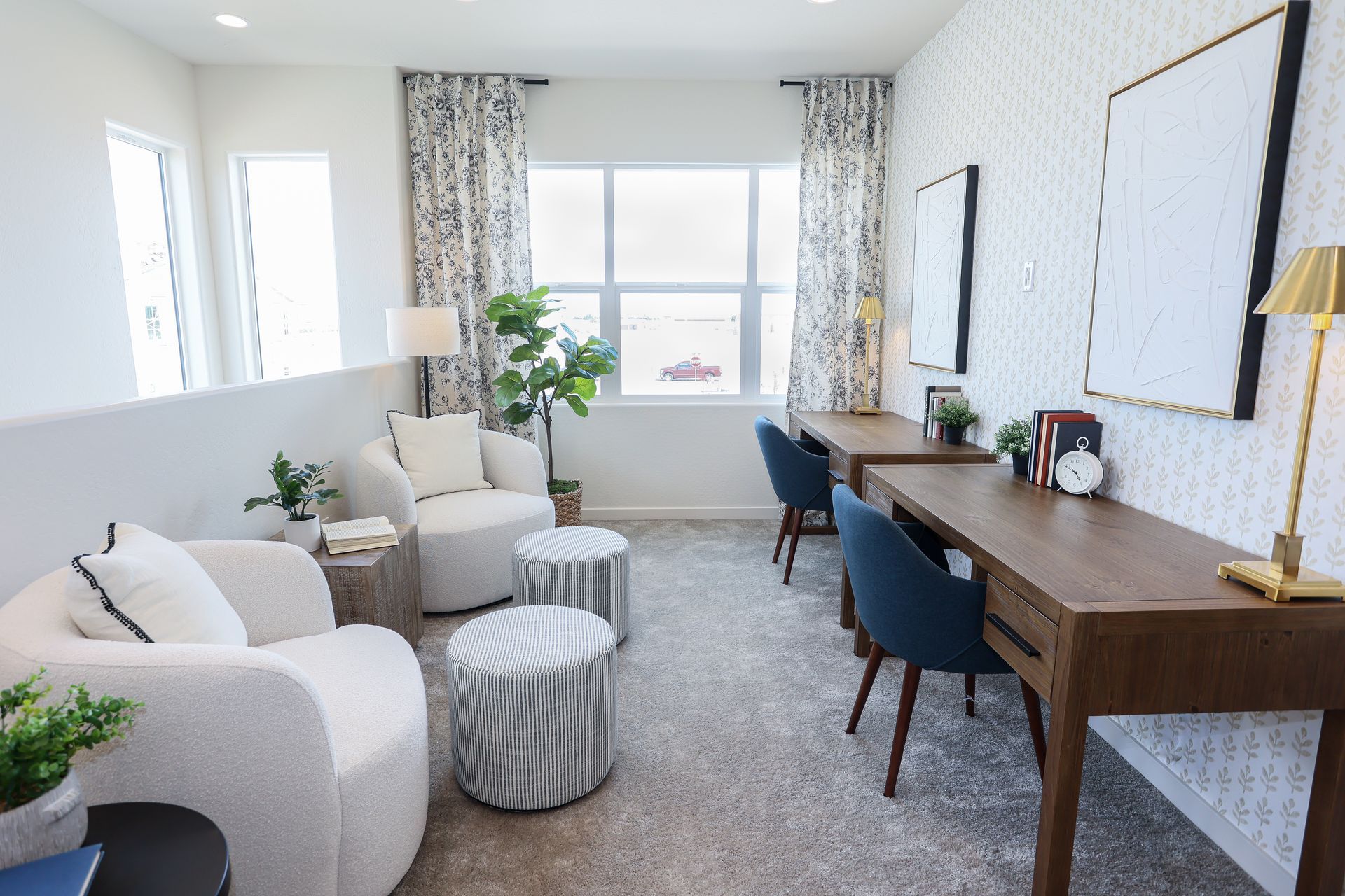 Bright living room with white sofa, striped ottoman, desk, chairs, and large window with curtains