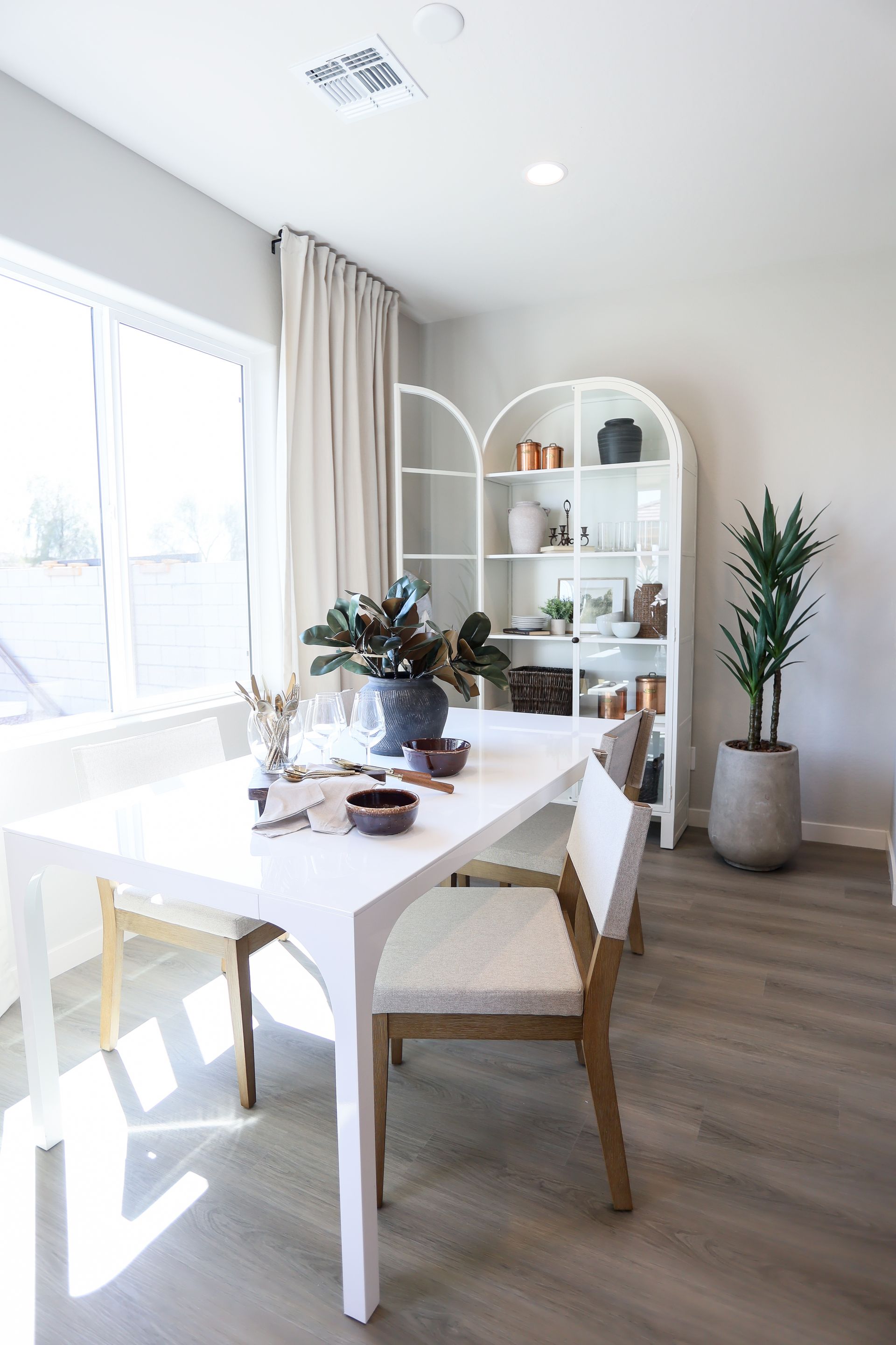 Bright dining room with white table, wicker chairs, large window, and a plant shelf