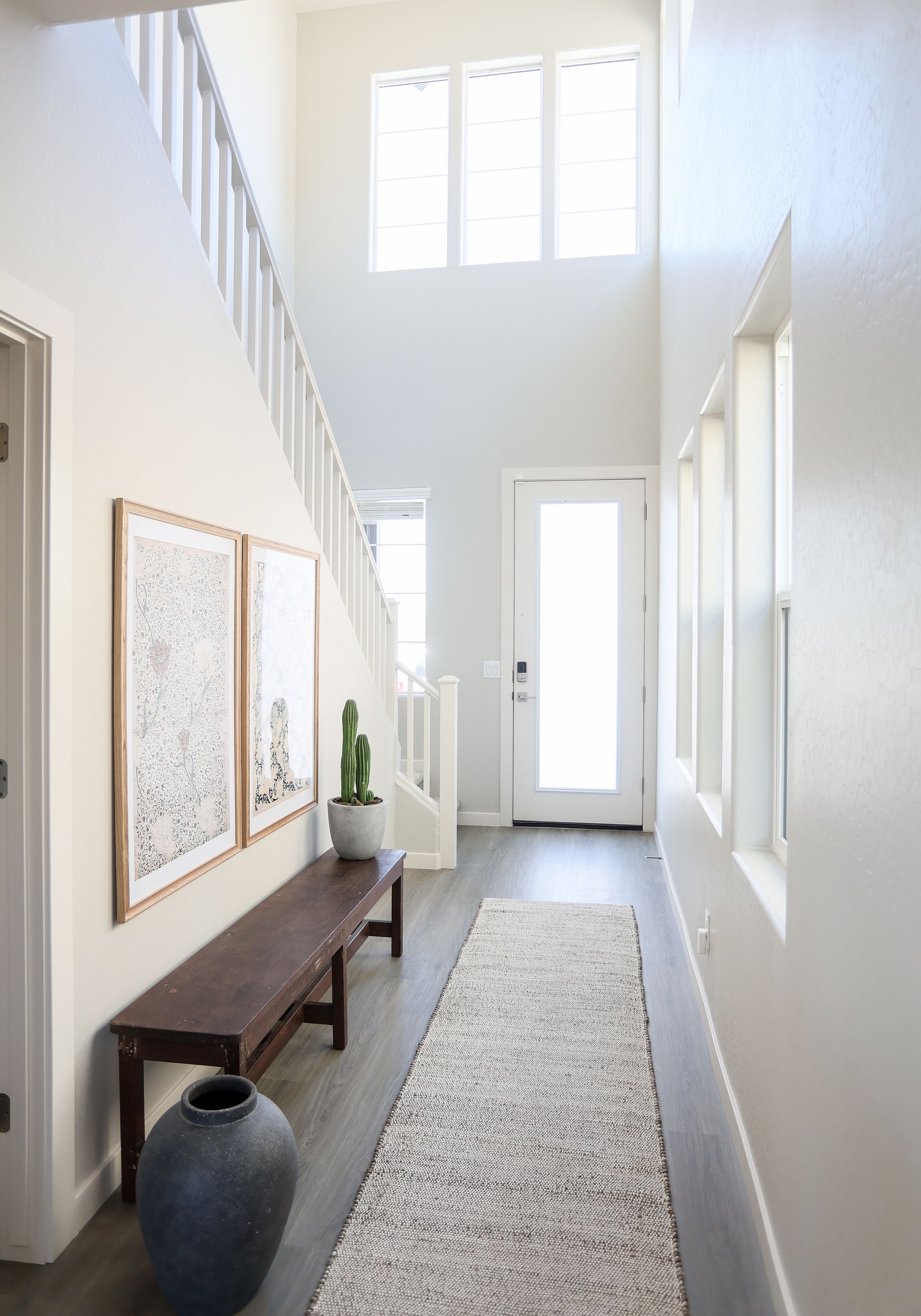 Bright white entry hall with a long runner rug, bench, wall art, and high windows letting in natural light