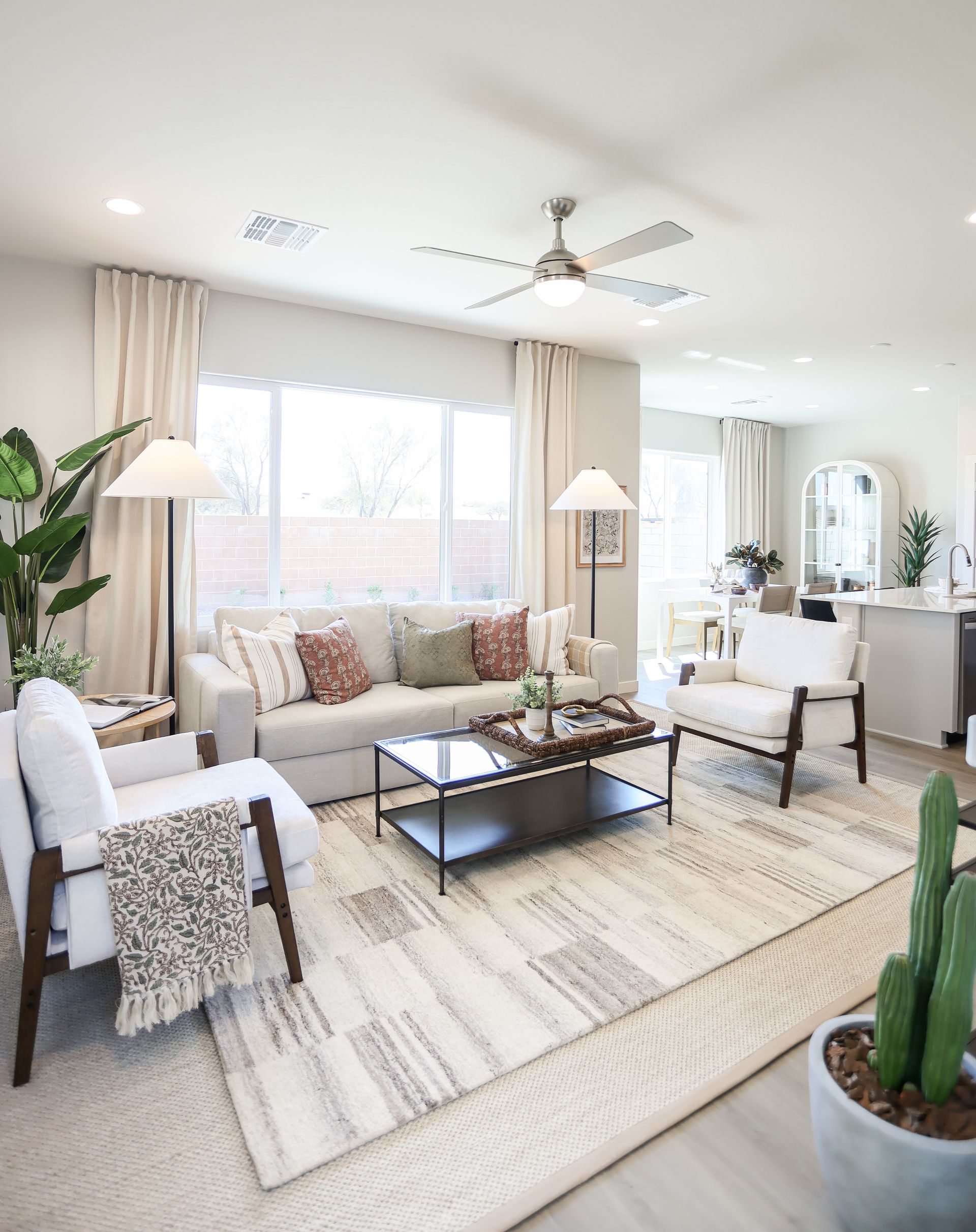 Bright living room with beige sofa, armchairs, coffee table, rug, and large window with sheer curtains
