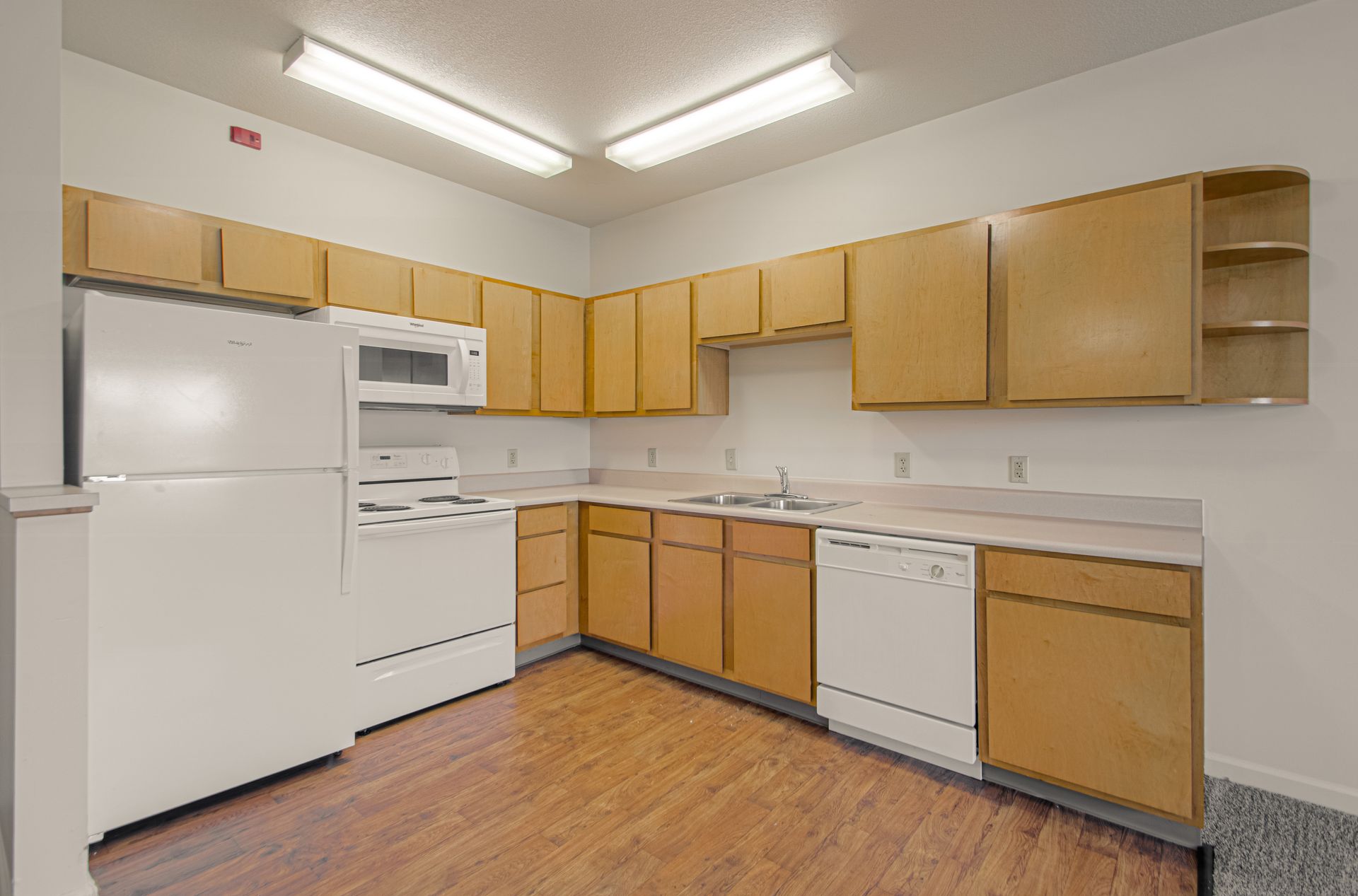 A kitchen with light wooden cabinets, white appliances, and a faux wood floor. It is brightly lit.