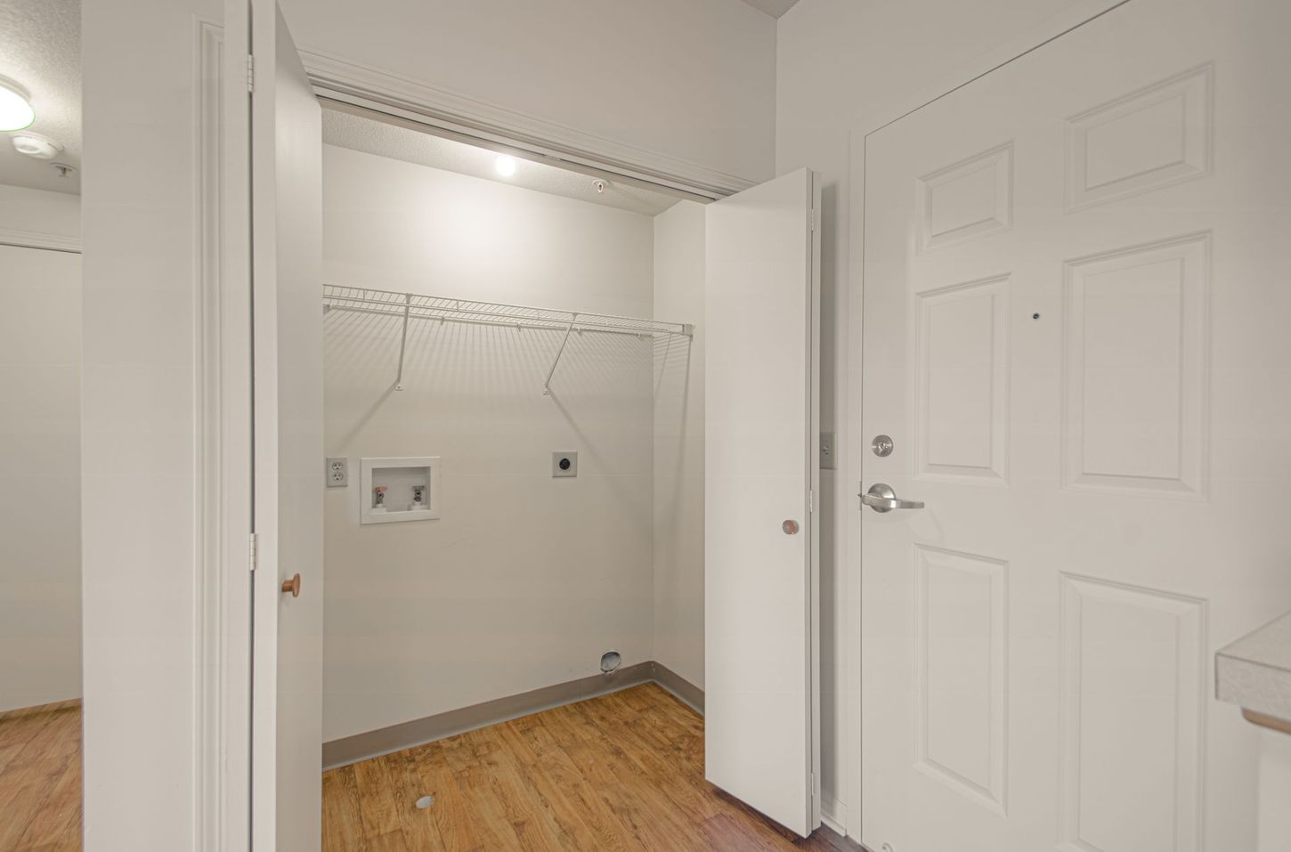 A small, white laundry room with a washing machine hookup, a clothes rack, and a closed door with a handle.