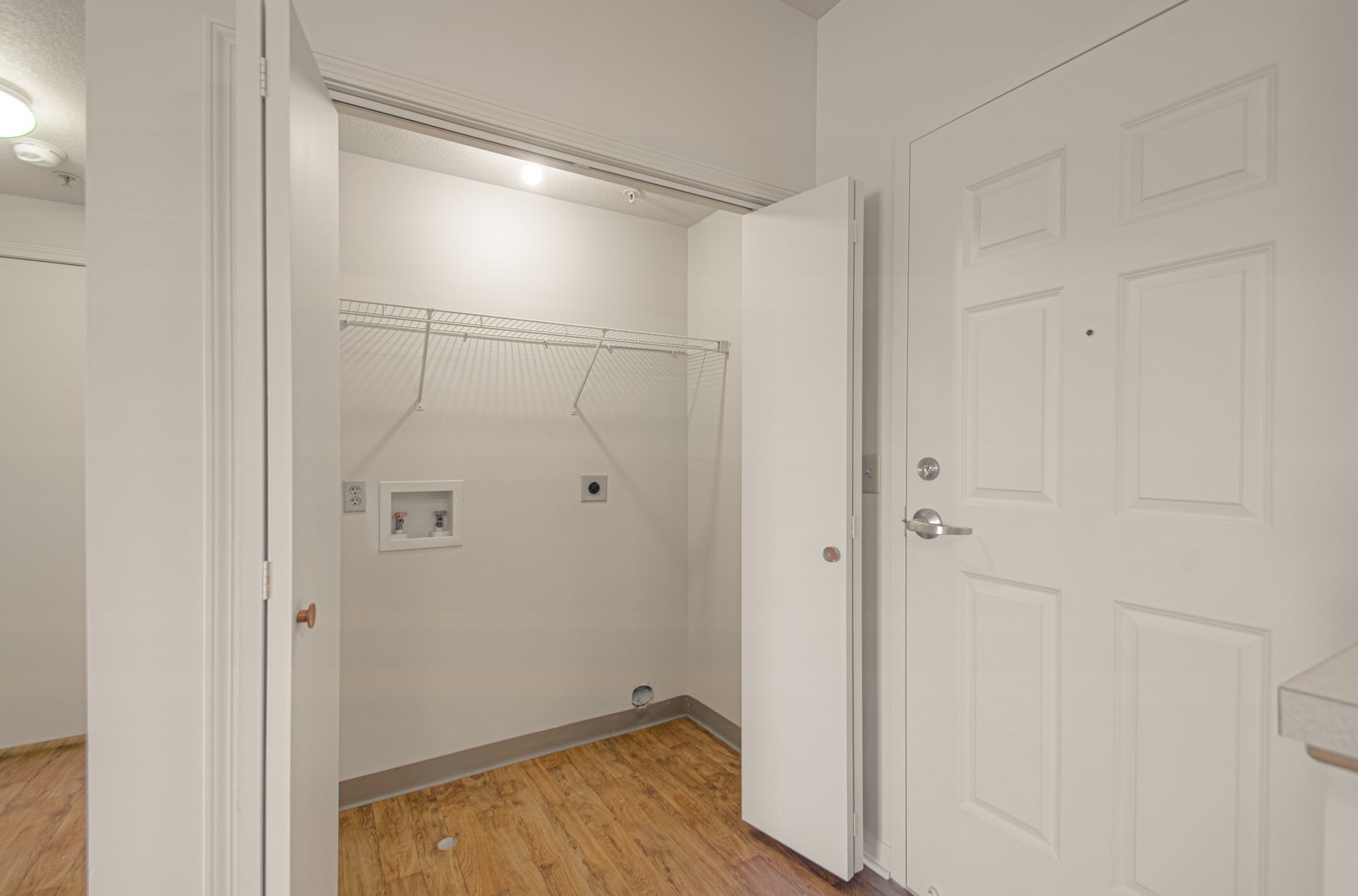A small, white laundry room with a washing machine hookup, a clothes rack, and a closed door with a handle.