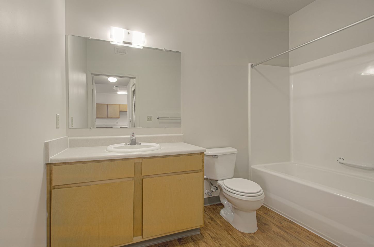 A bathroom with a vanity, toilet, and bathtub. The room has light-colored walls and flooring.