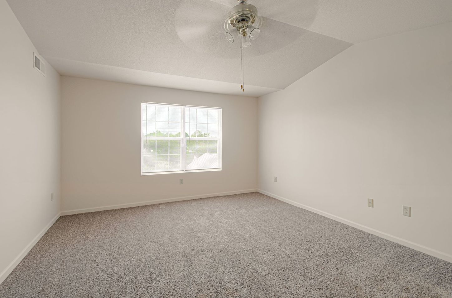 Empty bedroom with gray carpet, a window with sheer curtains, and a ceiling fan. White walls and trim.