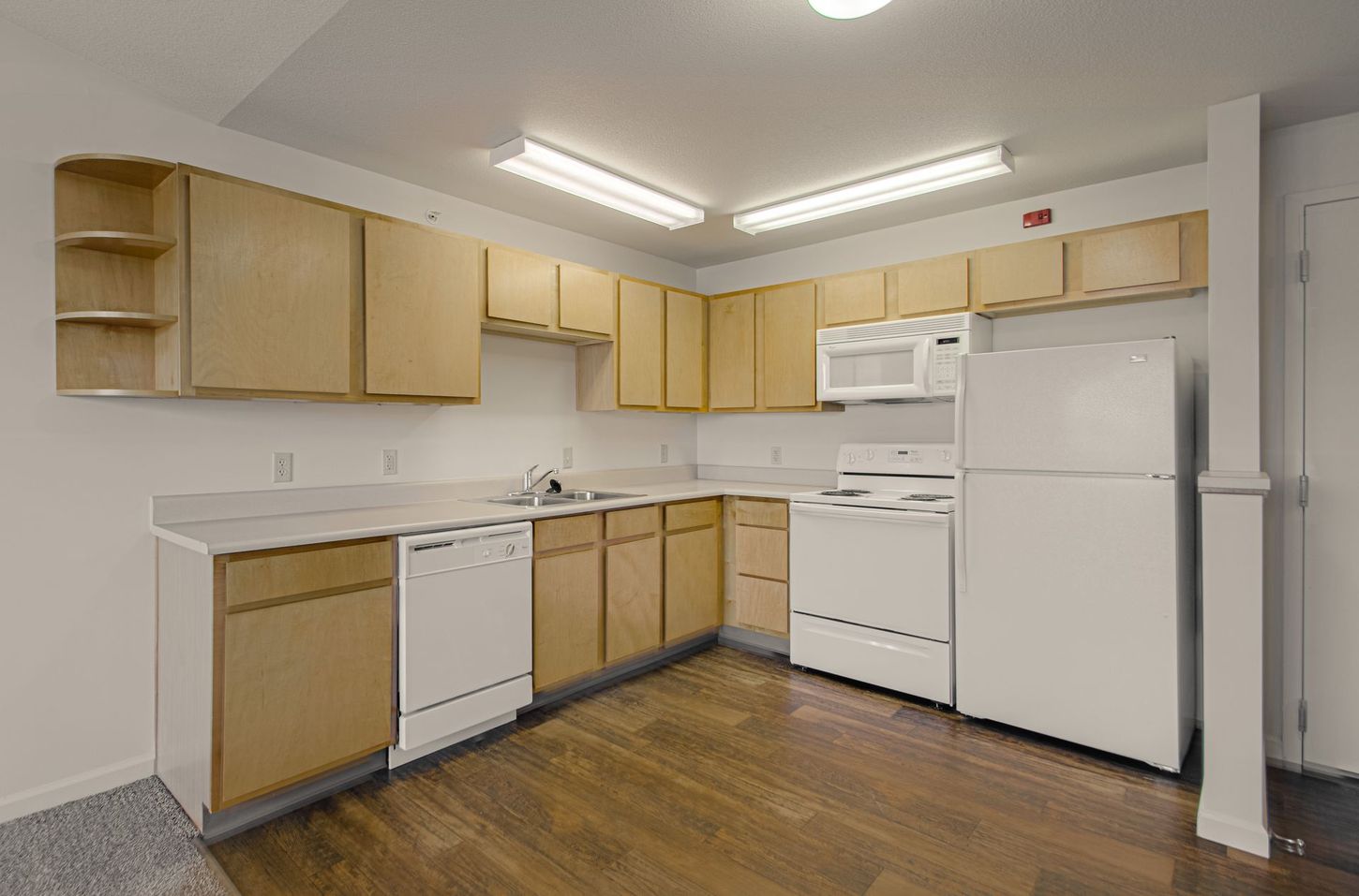 A kitchen with light wood cabinets and white appliances. Features a dishwasher, stove, refrigerator, and microwave.
