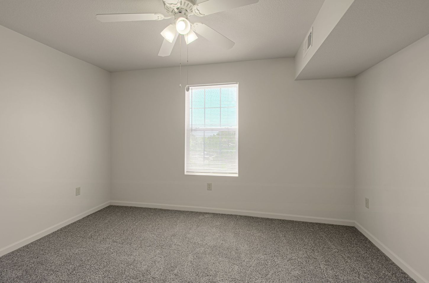Empty bedroom with gray carpet, white walls, a window with blinds, and a ceiling fan.