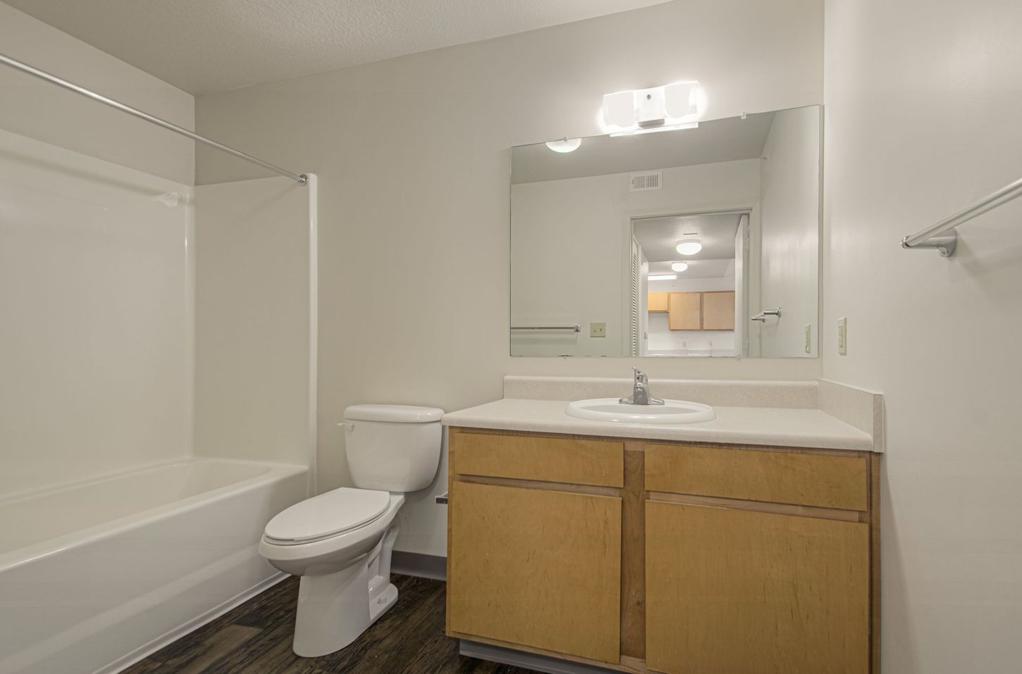 Bathroom with a white tub and toilet, light wood vanity with a sink, and a large mirror.