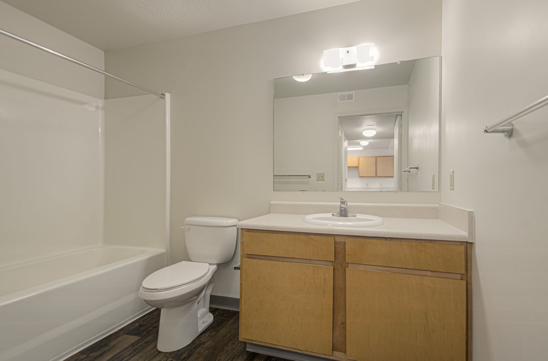 Bathroom with a white tub and toilet, light wood vanity with a sink, and a large mirror.