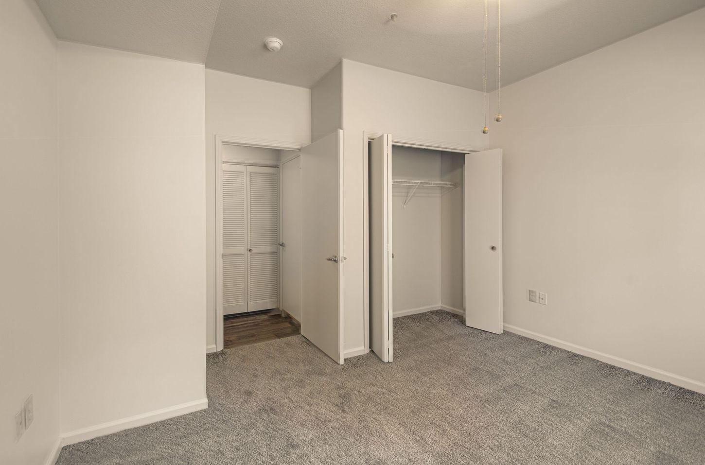 Empty bedroom with grey carpet, white walls, and two closets. One closet door is open.