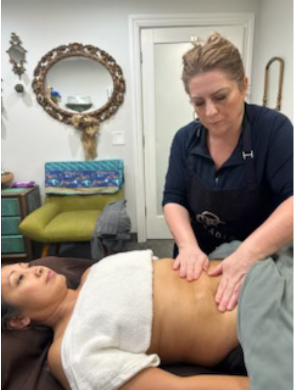Hands massaging a person's abdomen, partially covered by a towel, lying on a massage table.