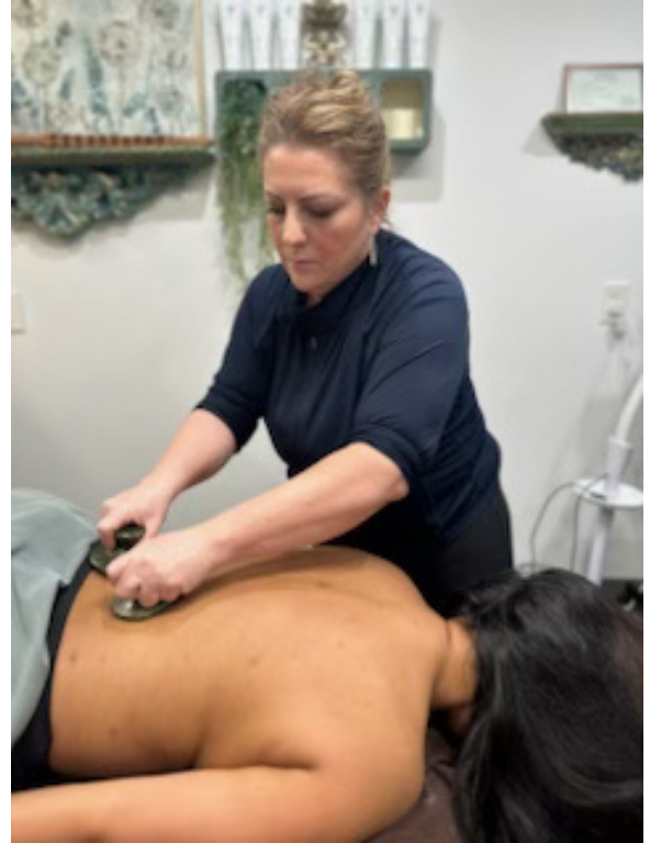 Hands massaging a person's lower back, lying face down on a massage table, covered by a white towel.