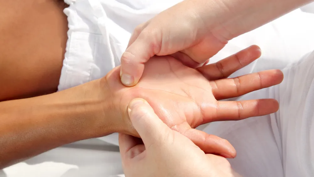Hands receiving a hand massage on a white surface; fingers applying pressure.