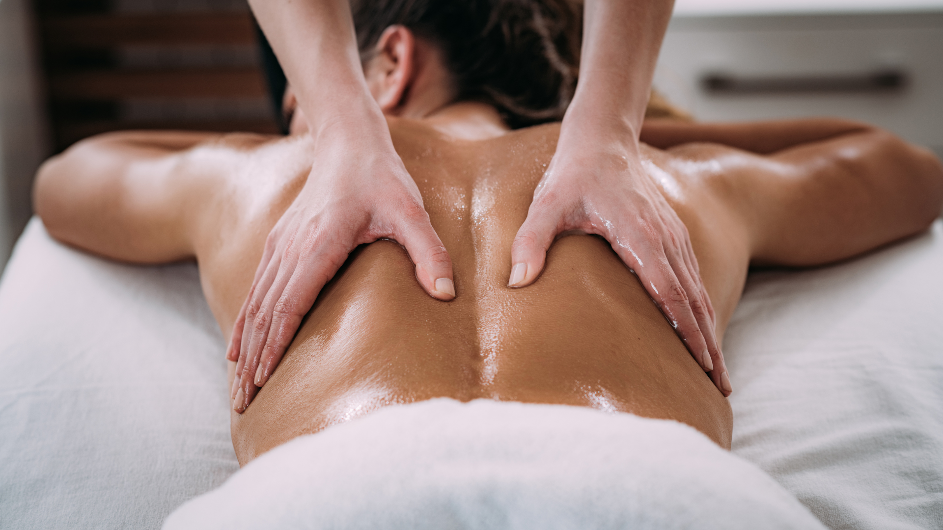 Person receiving a back massage on a massage table, hands on their back with oil.