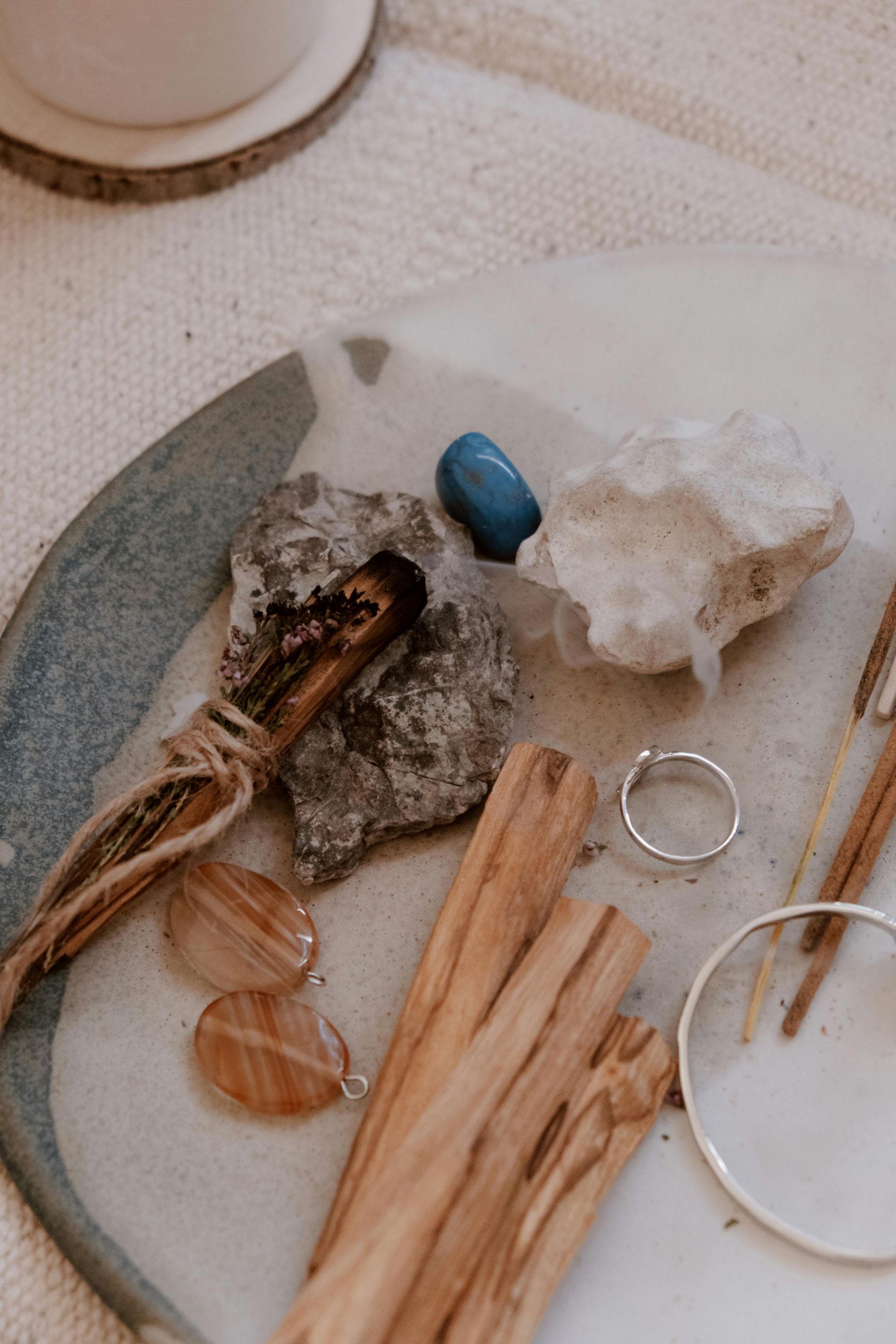 Arrangement of crystals, wood sticks, ring, magnifying glass, and other objects on a white and blue plate, top-down view.