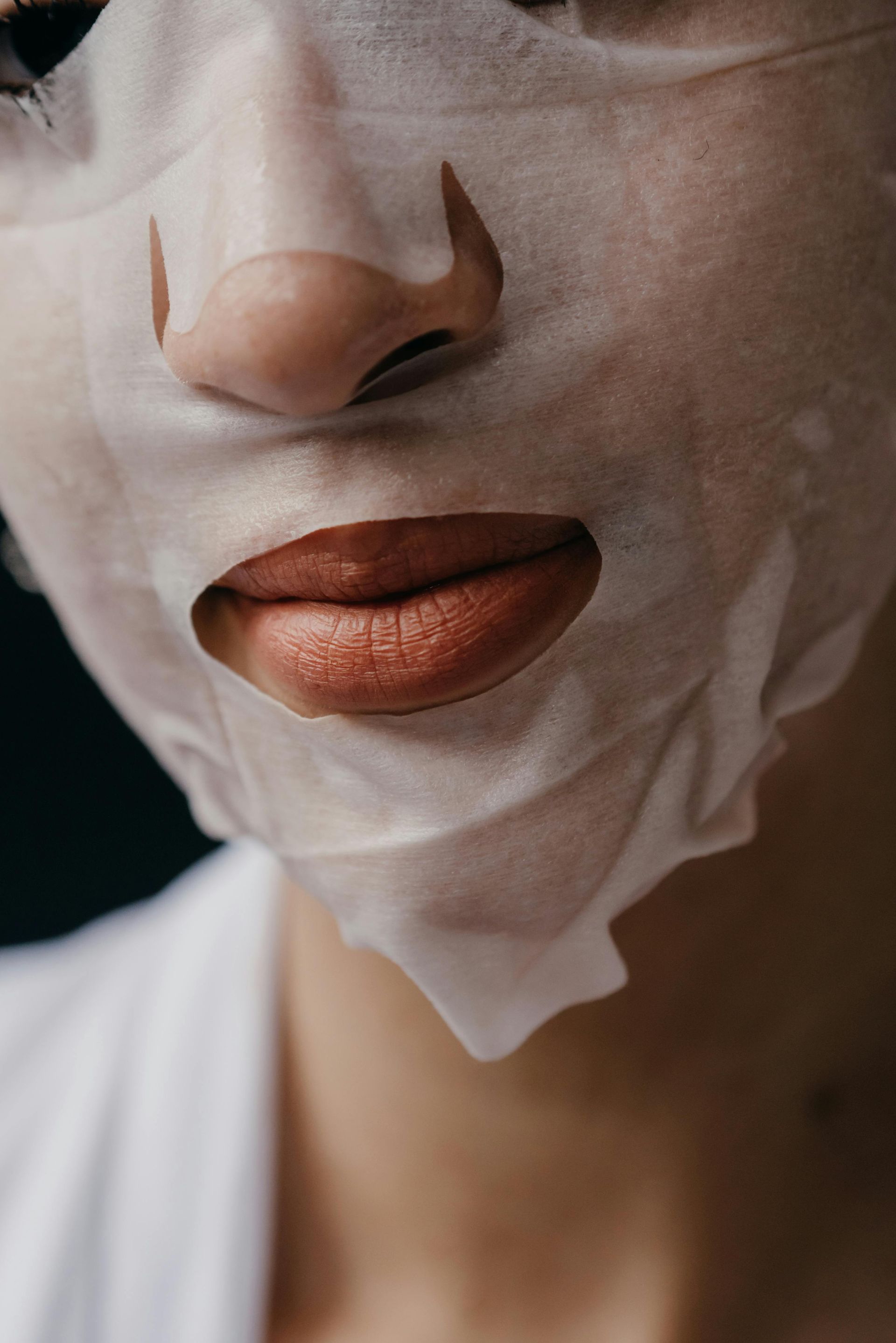 Close-up of a person's face wearing a white sheet mask over the nose and mouth.