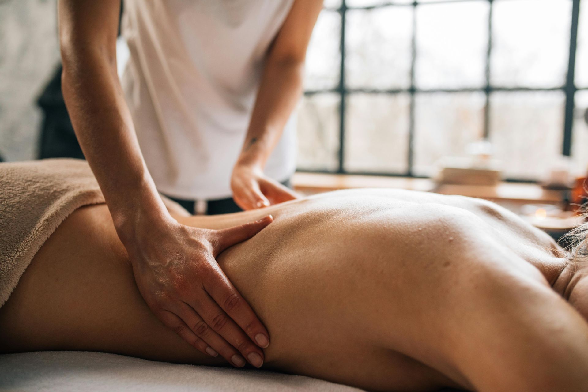 Person receiving a back massage in a room with a window. Hands apply pressure to the back.