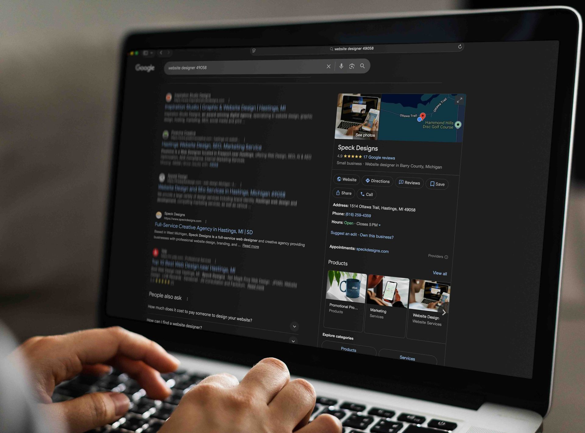 Person using a laptop with a dark-mode Google search open. Hands typing on the keyboard.