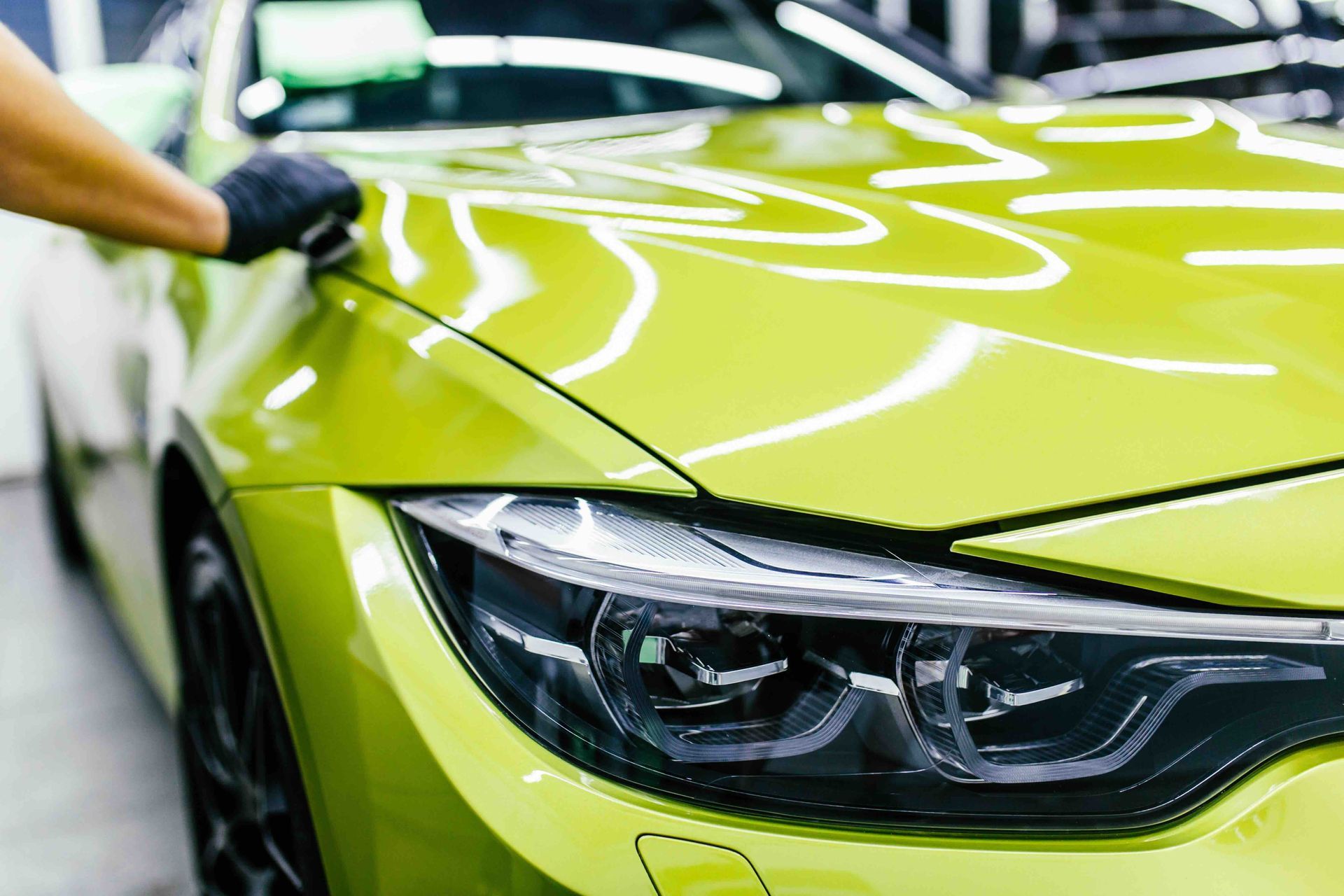 A person is polishing the hood of a green car.