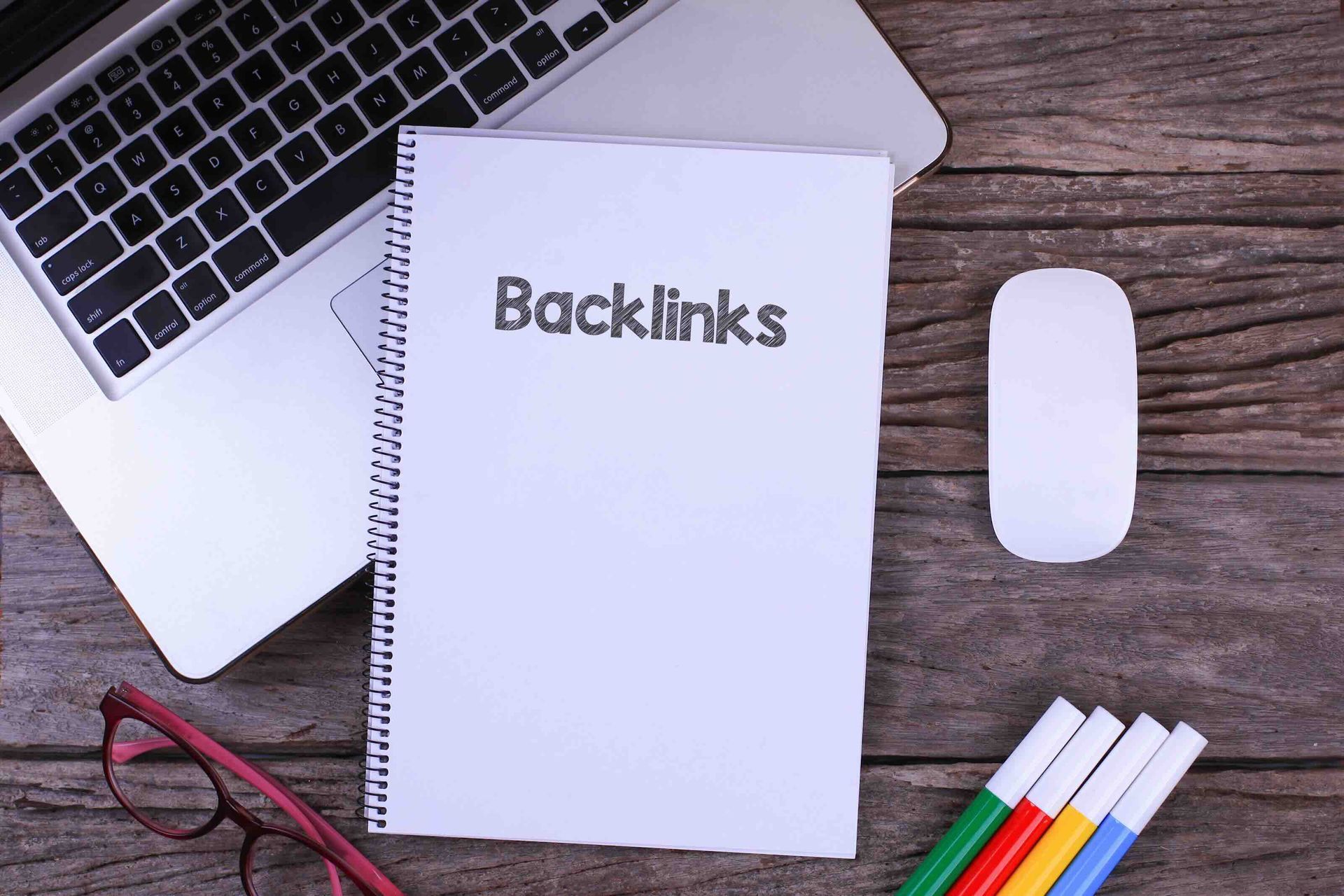 A notebook with the word backlinks written on it is sitting on a wooden table next to a laptop.