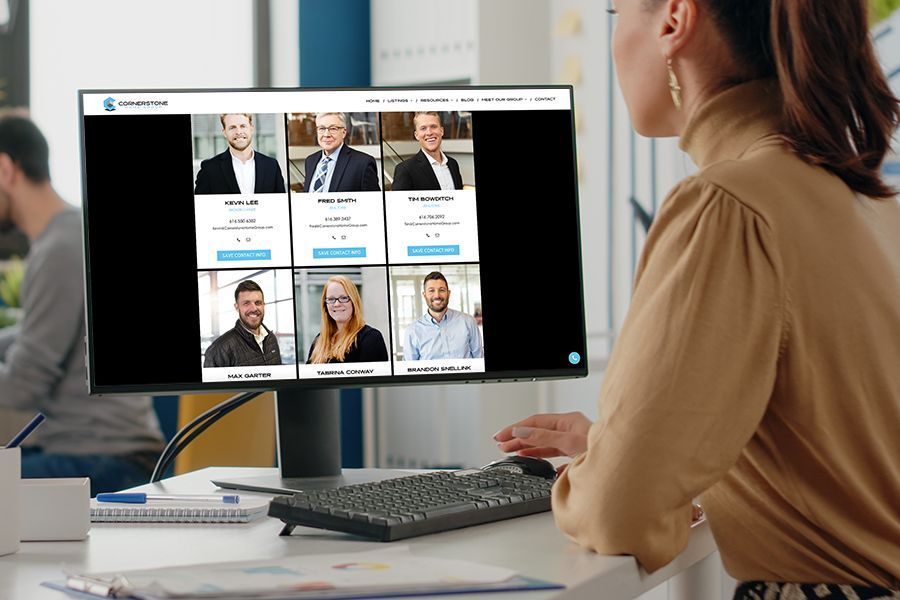 A woman is sitting at a desk in front of a computer monitor showing realtors of Cornerstone Home Group.