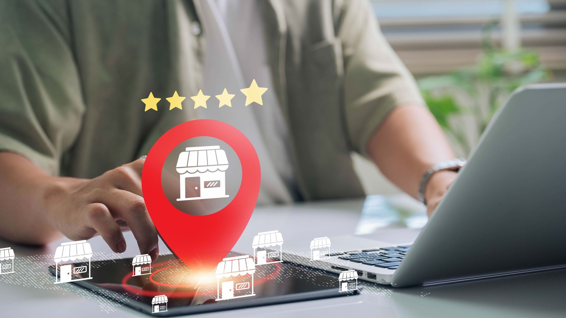 Hands using laptop next to glowing red map pin with store icon and five stars on a desk