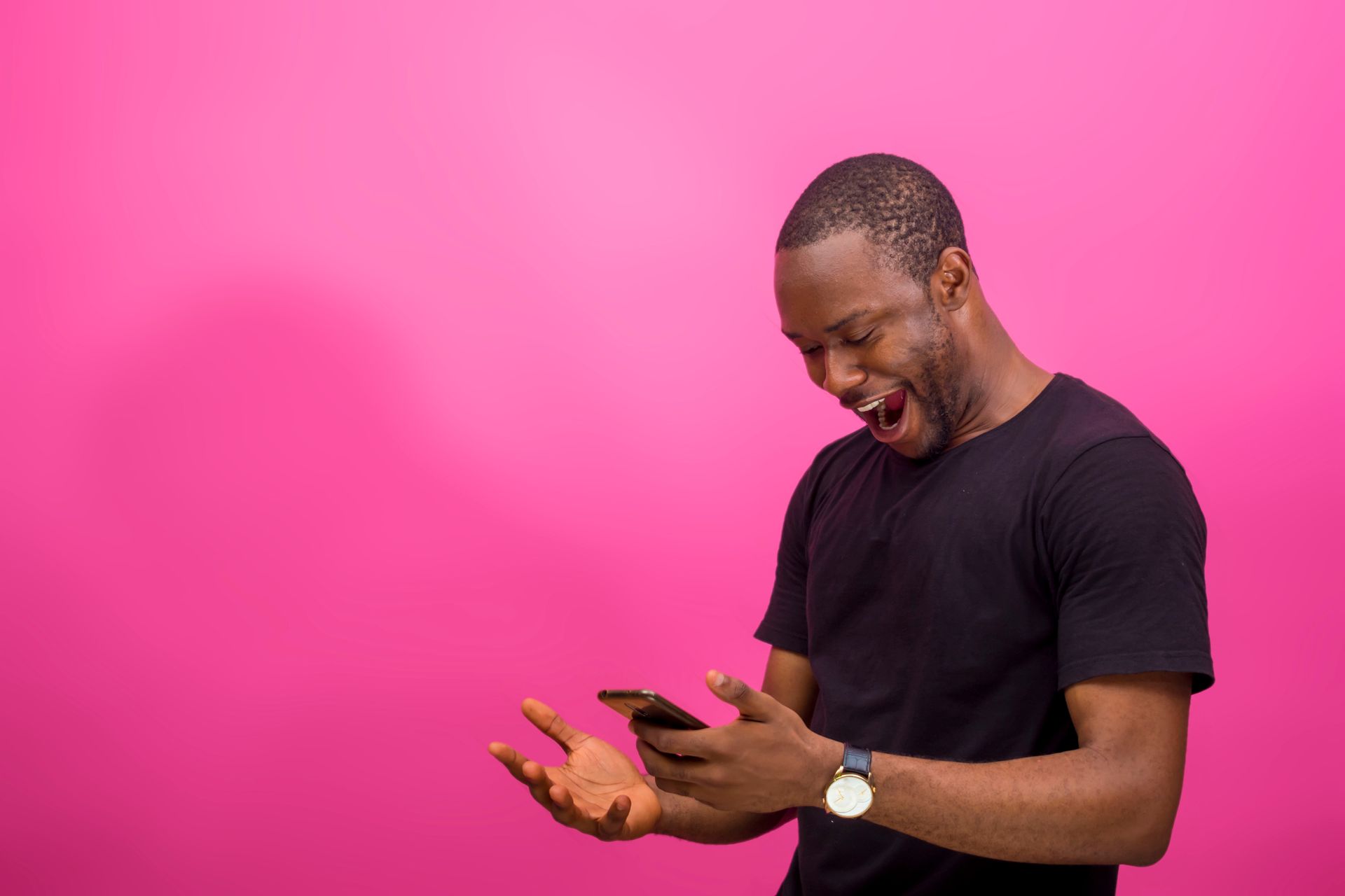 A man in a black shirt is looking at his cell phone on a pink background.