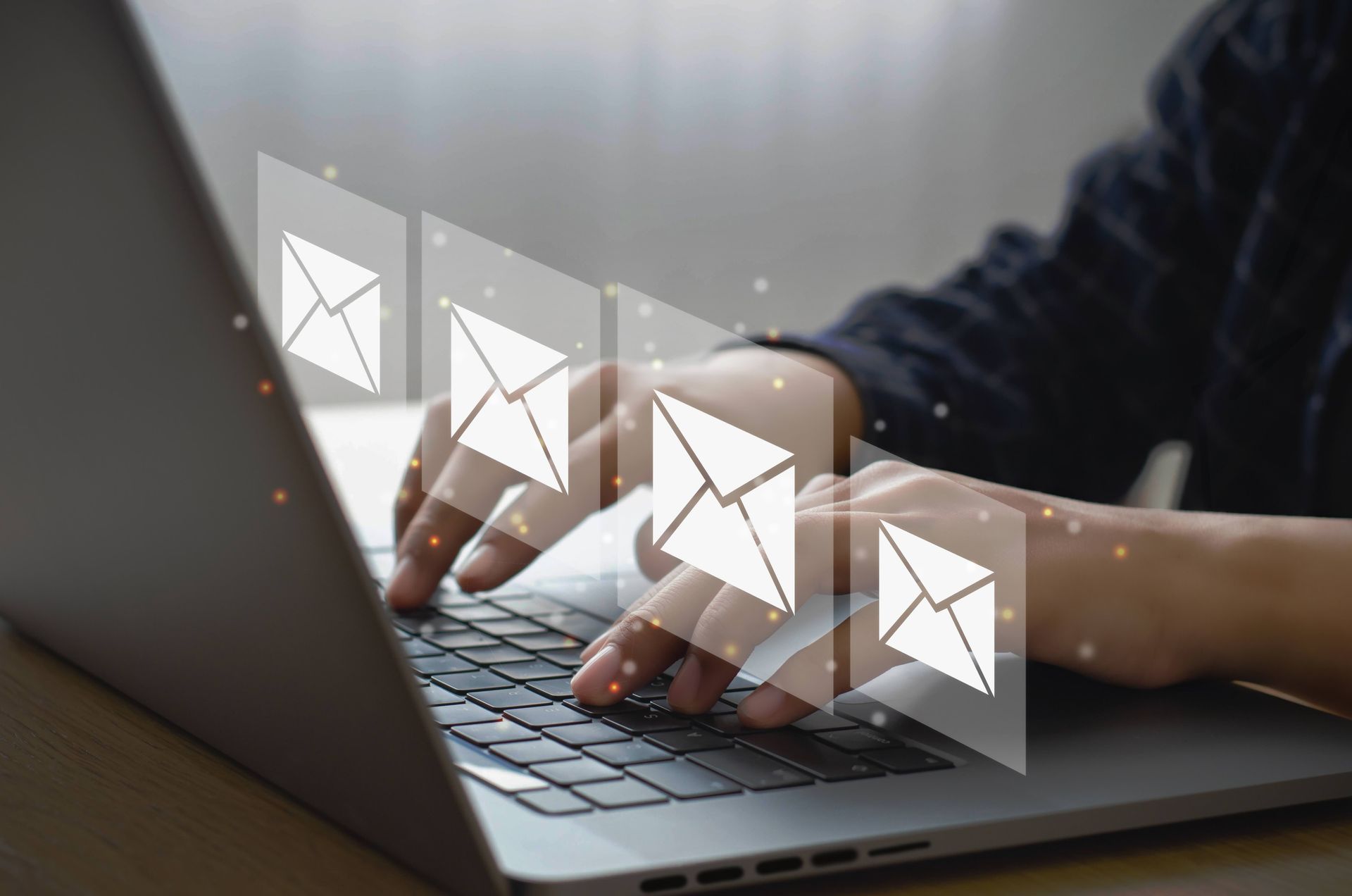 Person typing on laptop with email icons overlaid, symbolizing online communication.