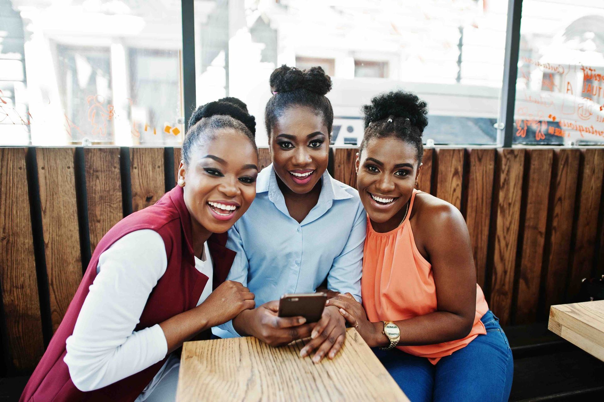 Three women are sitting at a table looking at a cell phone.