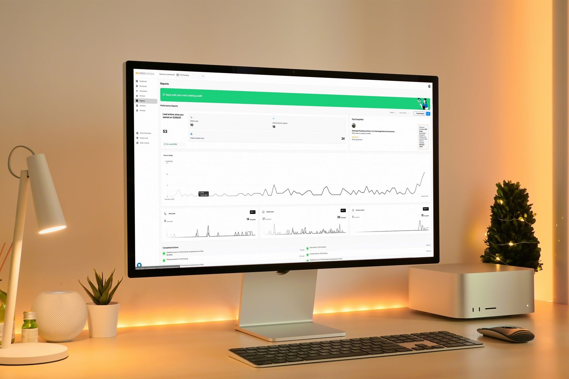 A computer monitor displays a data chart on a desk with a keyboard, lamp, and small Christmas tree.