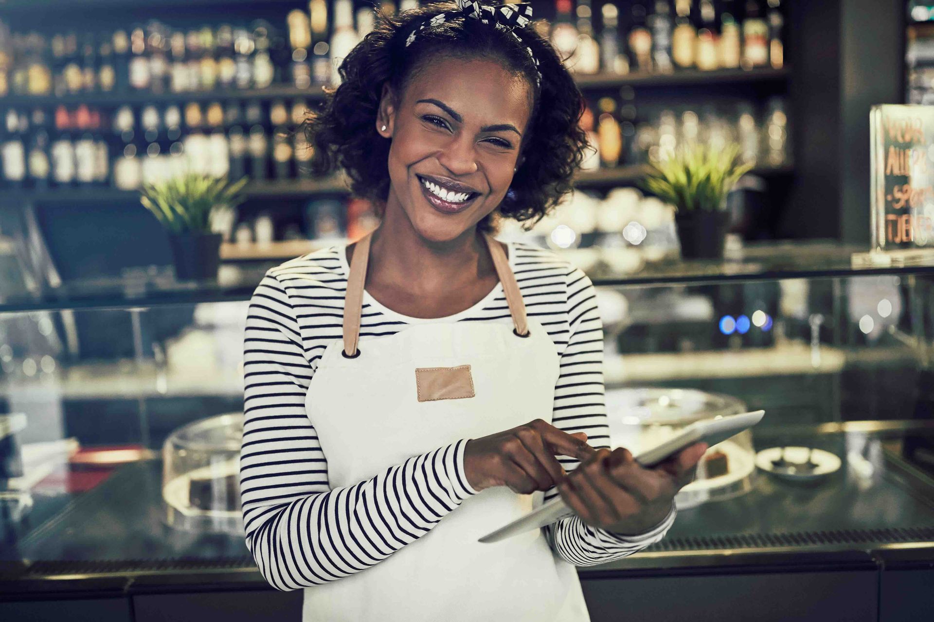 A woman is smiling while holding a tablet in a restaurant.