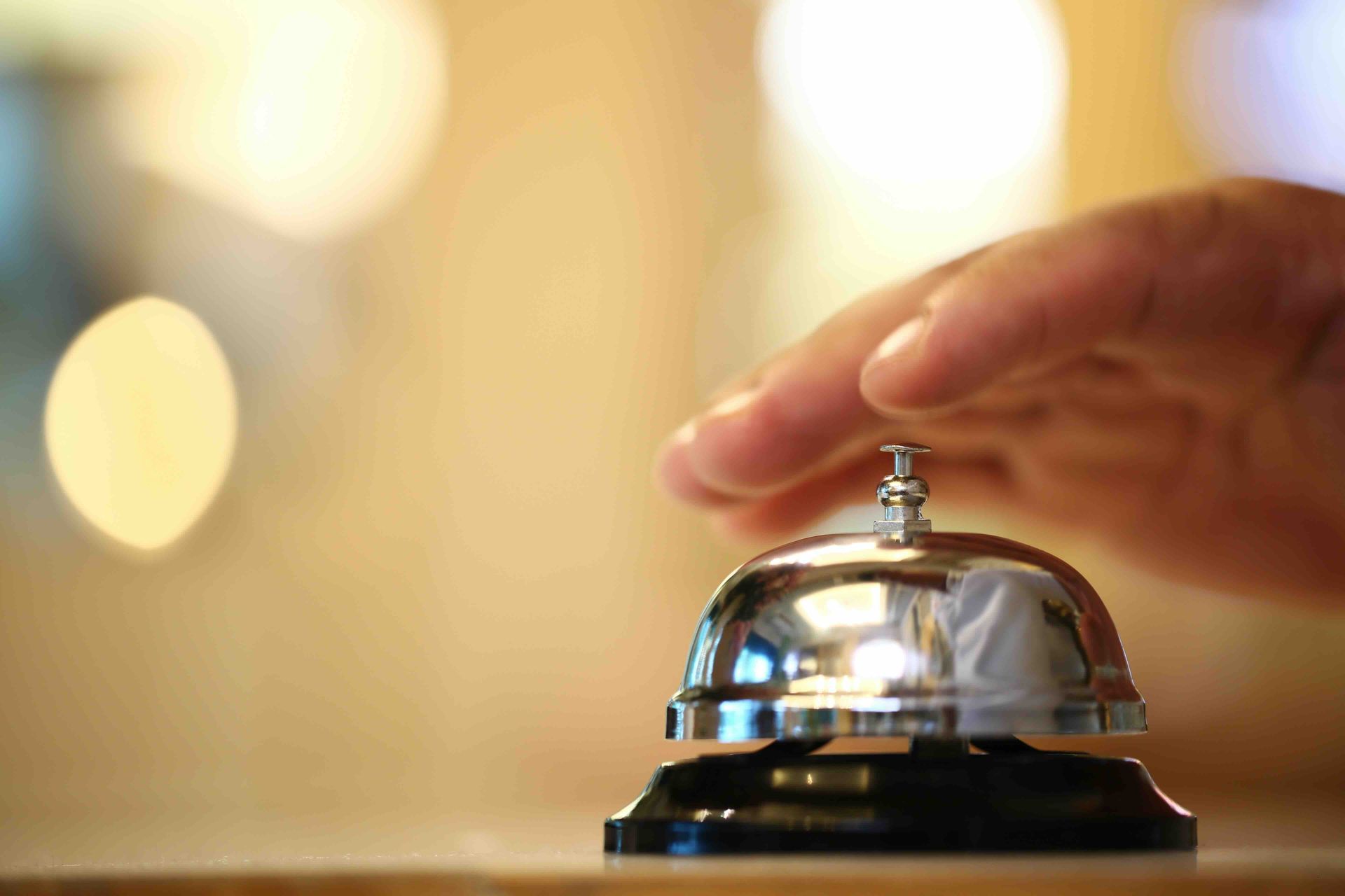 A person is pressing a hotel bell on a table.