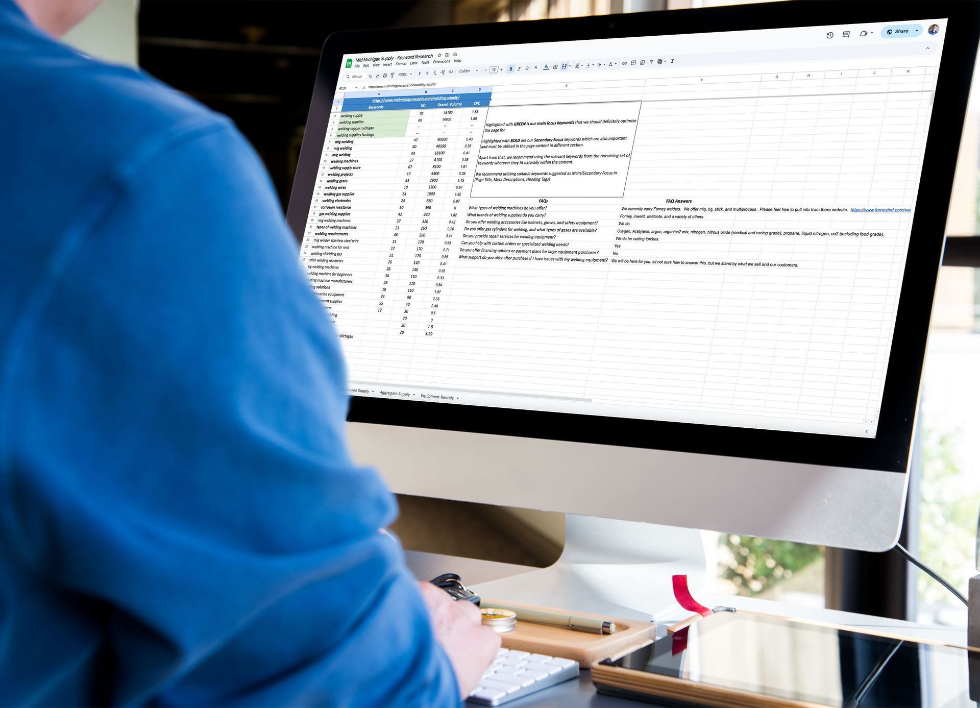 A man is sitting at a desk using a computer to create keywords and FAQs for a website.