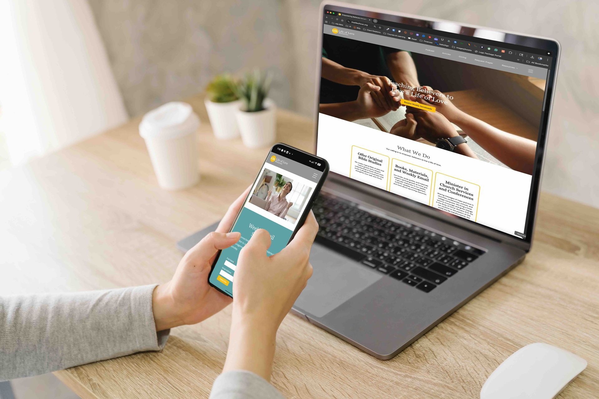 Person using a laptop and smartphone on a wooden desk; both devices display the sLOL Ministries website.