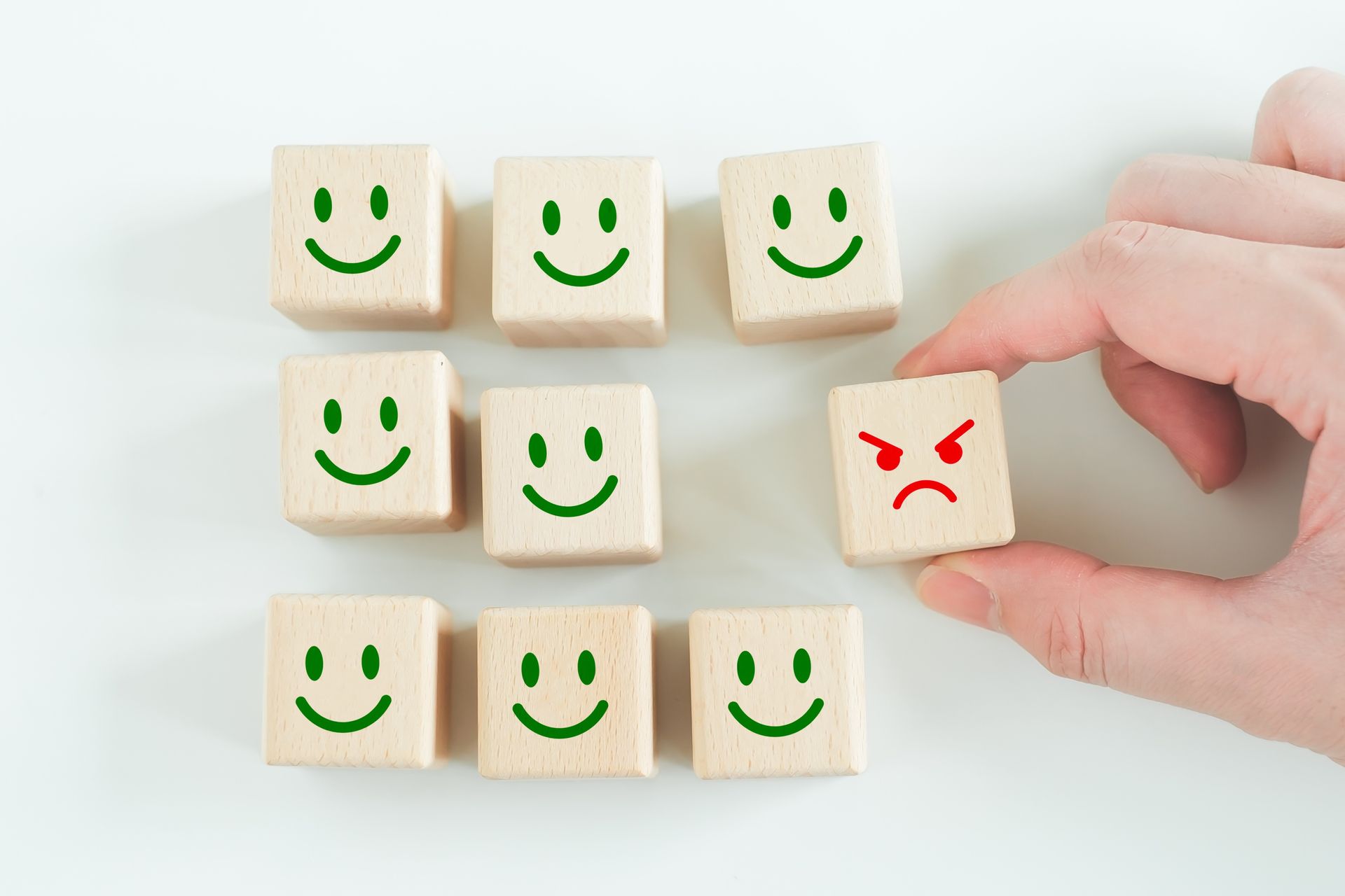 A person is holding a wooden block with a mad face on it surrounded by smiley face blocks.