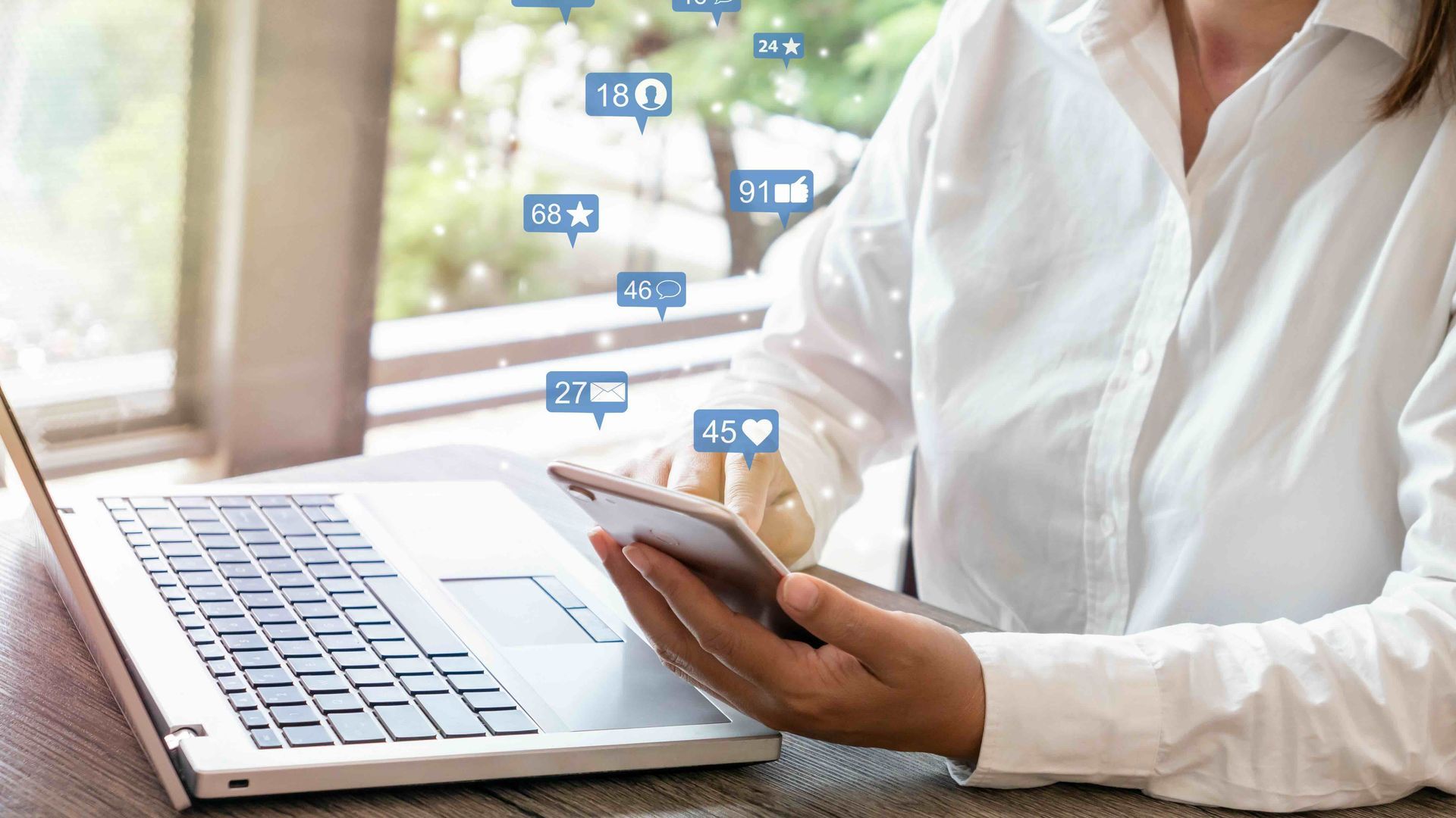 A woman is sitting at a table using a laptop and a phone.