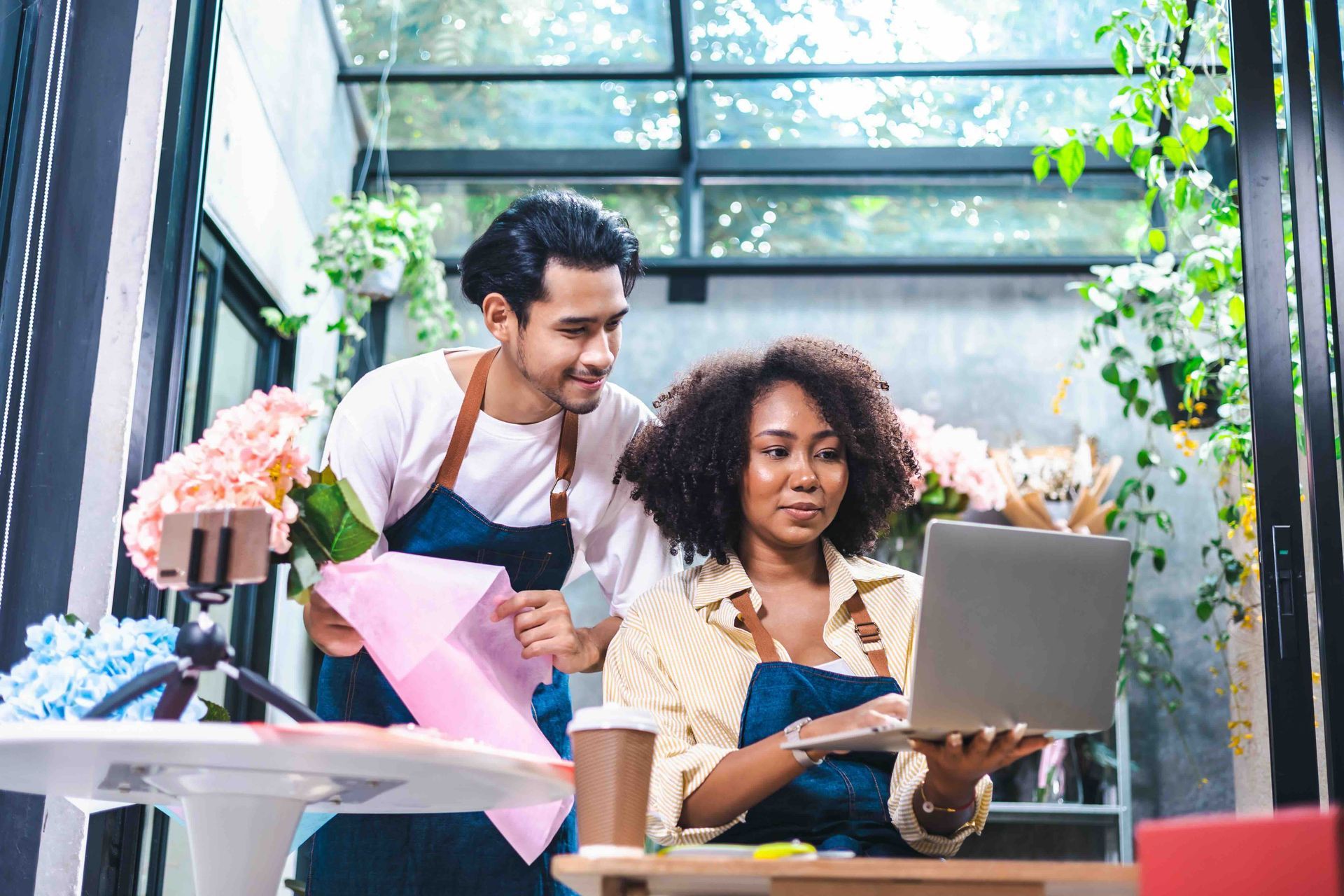 A man and a woman are working in a flower shop and looking at a laptop.