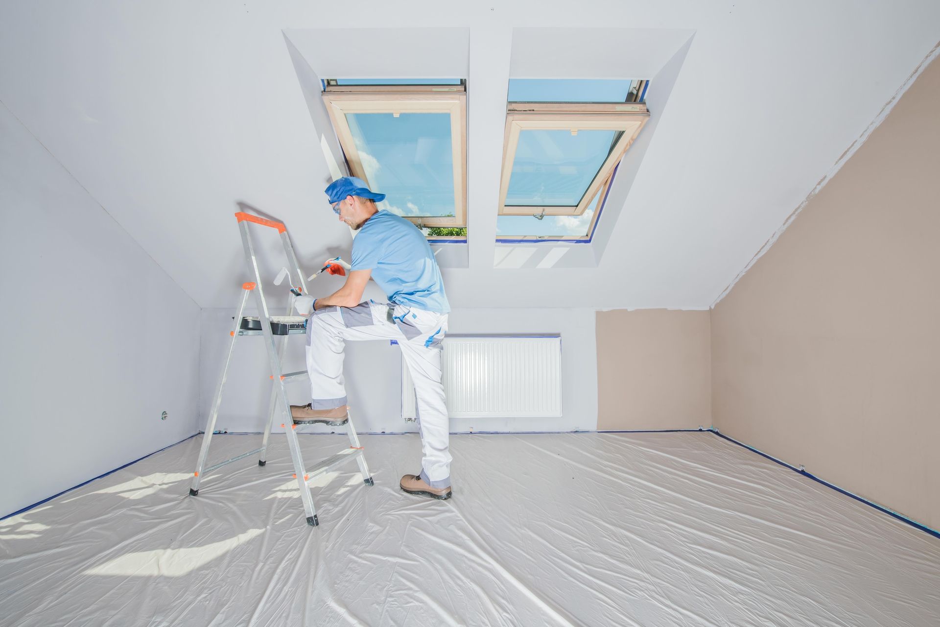 A man is standing on a ladder in an empty room painting the ceiling.