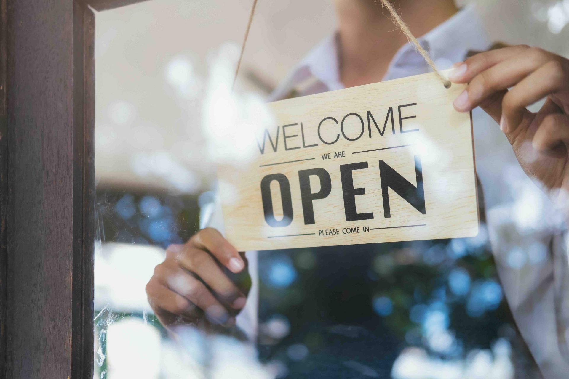 A man is holding a welcome open sign in front of a glass door.