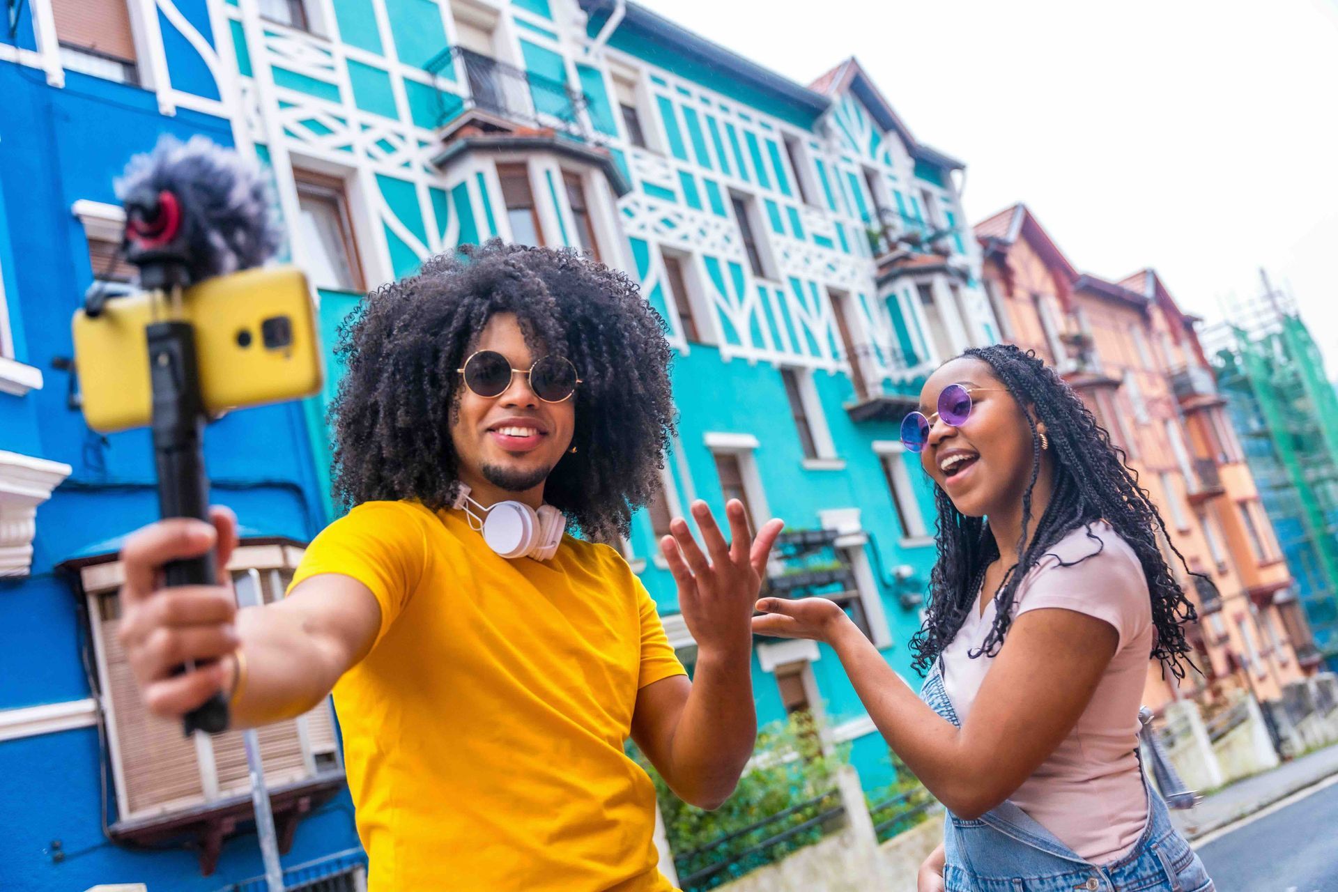 Two young people vlogging in front of colorful buildings.