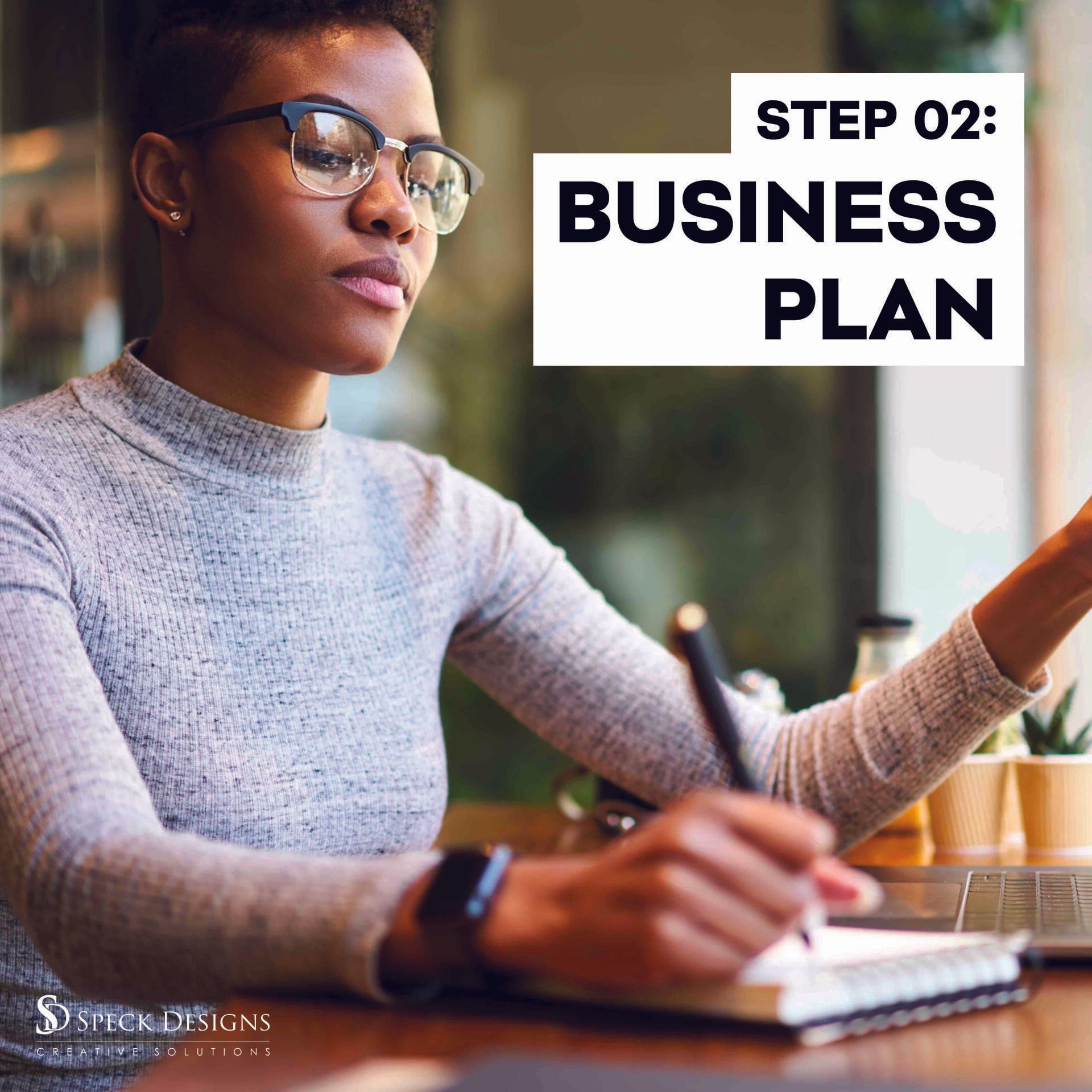 A woman wearing glasses is sitting at a table writing in a notebook.