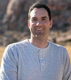 Steven, the owner of Speck Designs, is smiling for the camera in front of mountains in Nevada.