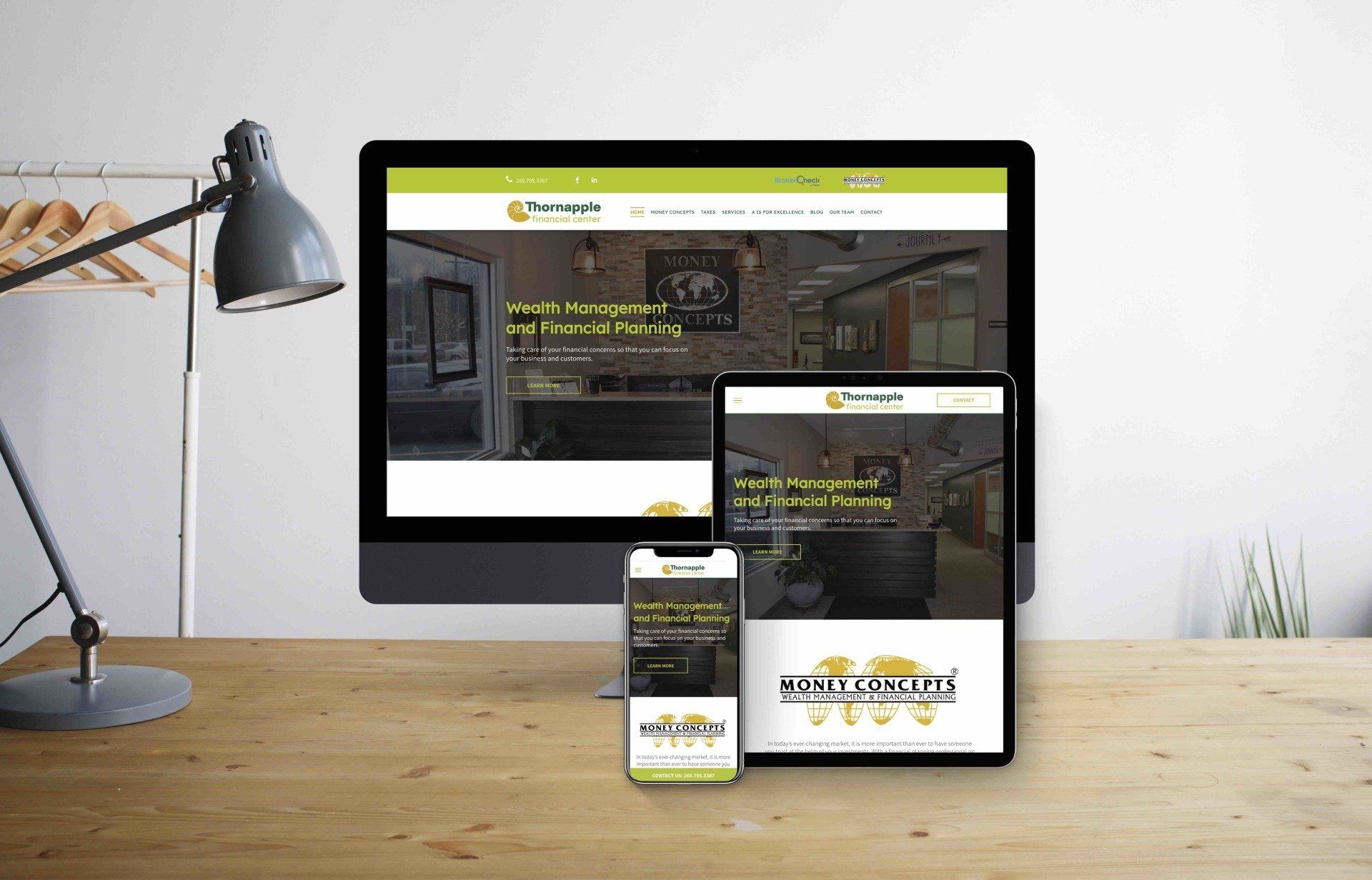 A computer, tablet, and cell phone are sitting on a wooden desk all showing the website for Thornapple Financial Center.