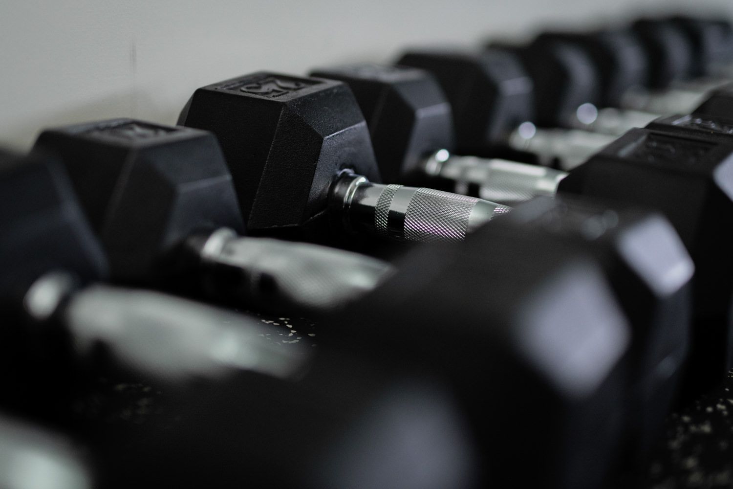 Black hexagonal dumbbells lined up on a rack in a gym setting.